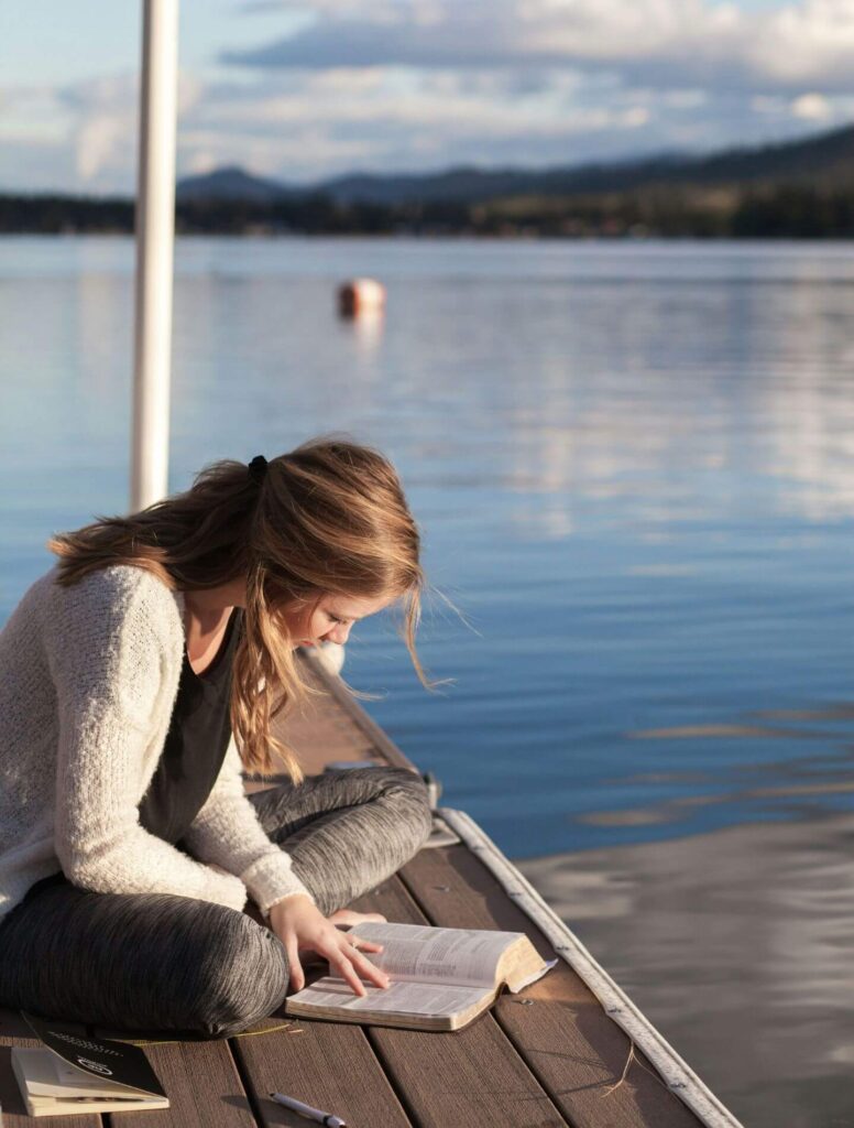 Girl reading a book while sitting on a dock by the water