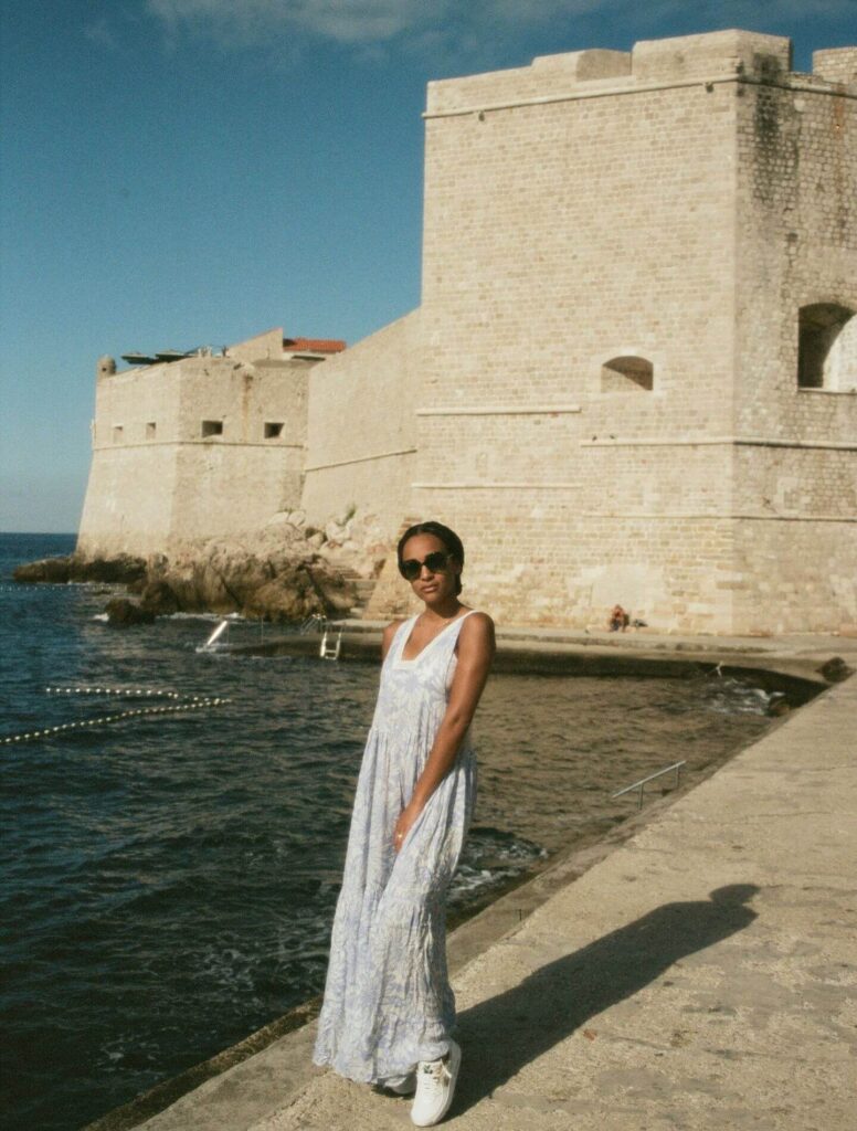 Woman wearing maxi dress by the water in front of a fort
