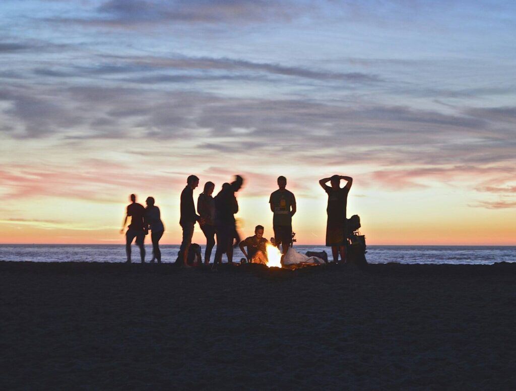 You adults around a fire on a beach at sunset